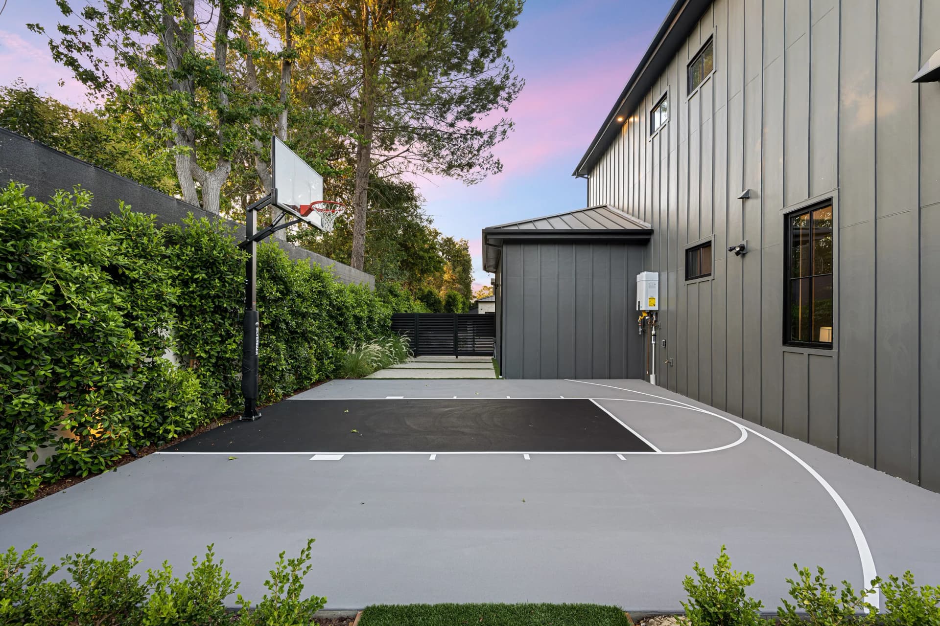 Finished half-court basketball court with regulation striping and installed hoop on a concrete slab in a residential yard.